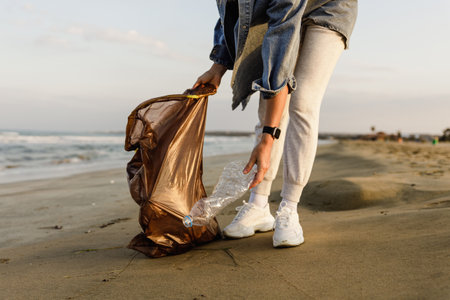 Woman volunteer is collecting plastic waste on the beach to contribute to the effort of keeping nature clean. Closeup of hand with plastic bottleの写真素材