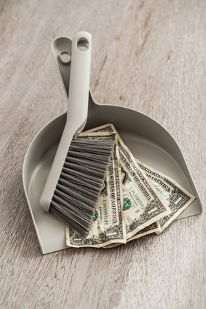 Dustpan and brush alongside scattered one-dollar bills on the floorの写真素材