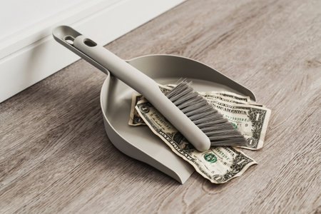 Dustpan and brush alongside scattered one-dollar bills on the floorの写真素材