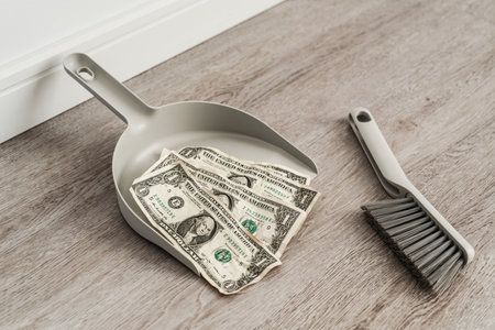 Dustpan and brush alongside scattered one-dollar bills on the floorの写真素材