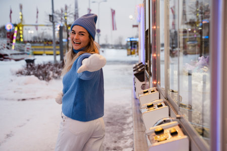 Cheerful and stylish woman, dressed in warm clothes, is having fun in a snowy winter amusement parkの写真素材