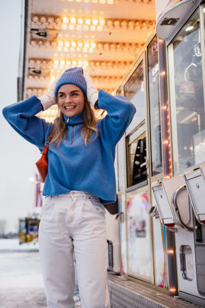 Cheerful and stylish woman, dressed in warm clothes, is having fun in a snowy winter amusement parkの写真素材