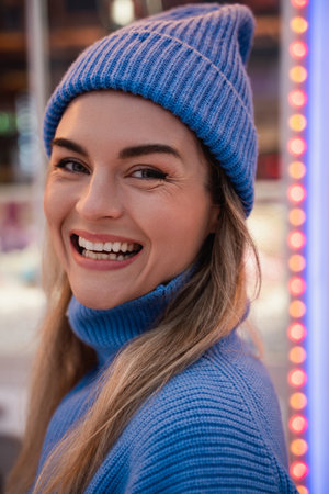 Cheerful and stylish woman, dressed in warm clothes, is having fun in a snowy winter amusement parkの写真素材