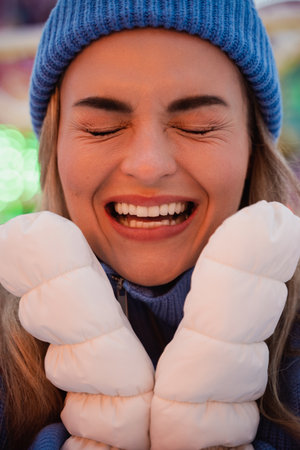 Cheerful and stylish woman, dressed in warm clothes, is having fun in a snowy winter amusement parkの写真素材