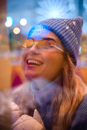 Woman, dressed in warm clothes and wearing sunglasses shaped like fire flames, is having fun in a amusement parkの写真素材
