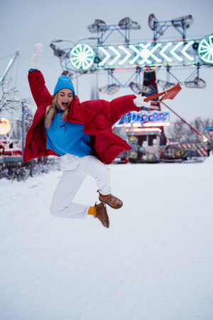 Cheerful and stylish woman, dressed in warm clothes, is having fun in a snowy winter amusement park