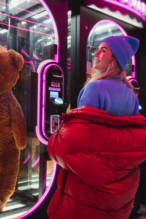 Cheerful and stylish woman, dressed in warm clothes, is having fun in a snowy winter amusement parkの写真素材