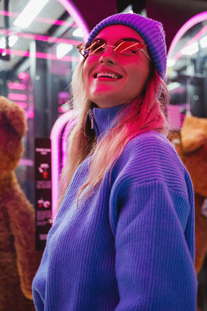 Cheerful and stylish woman, dressed in warm clothes and wearing sunglasses shaped like fire flames, is having fun in a snowy winter amusement parkの写真素材