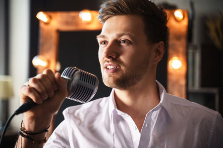 Young man with microphone is singing at homeの写真素材