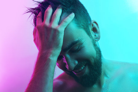 Handsome young man with wet skin in neon lightの写真素材