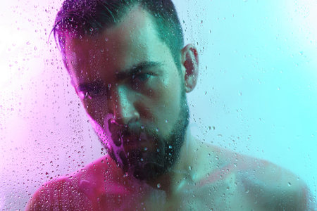 Portrait of handsome young man captured through wet glass in colorful light