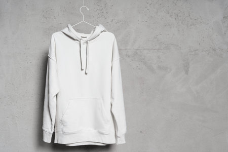 Blank white hoodie hanging on the thin metallic hanger against a concrete wall