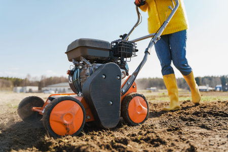 Young woman villager is using aerator machine to scarification and aeration of lawn or meadow