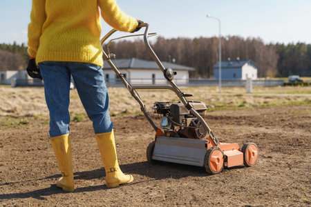 Young woman villager is using aerator machine to scarification and aeration of lawn or meadow