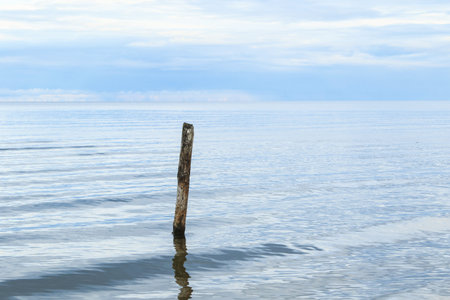 A beautiful shot of a calm sea scenery with a pole sticking out of water on horizon background.