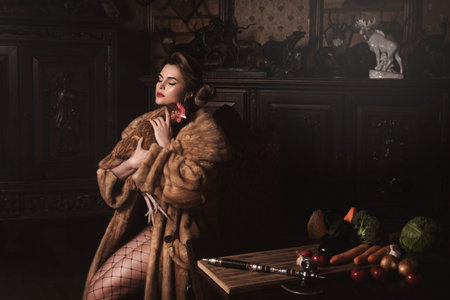 Provocative image of gorgeous woman wearing fur coat is holding hen.
