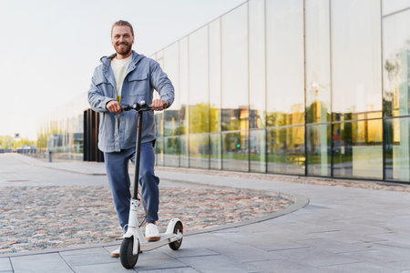Portrait of young cheerful man riding his e-scooter on the city street