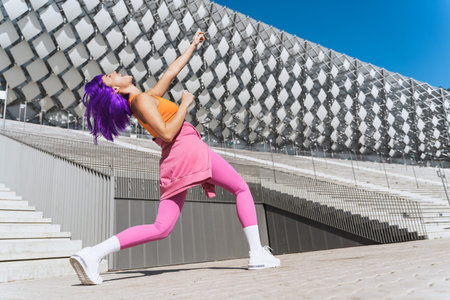 Carefree active woman dancer wearing colorful sportswear having fun on the street during sunny day