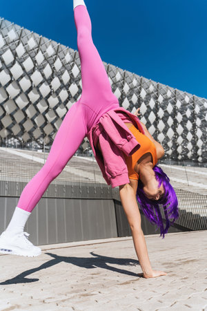 Carefree young woman wearing colorful sportswear making cartwheel movement on the street