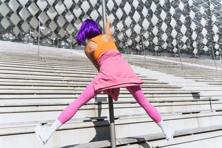 Carefree woman dancer wearing colorful sportswear having fun on the pole during summer day
