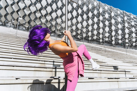 Carefree woman dancer wearing colorful sportswear having fun on the pole during summer day