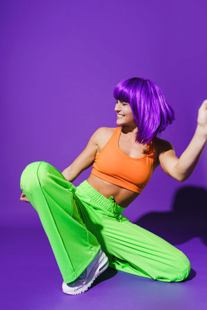 Carefree active woman dancer wearing colorful sportswear performing against purple background