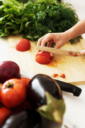 Closeup of female hands with knife slicing red tomato on wooden cutting boardの写真素材