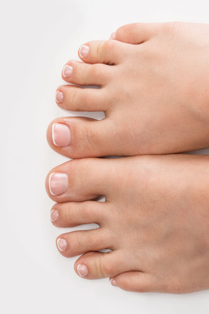Closeup of female feet with soft skin and french pedicure on white background
