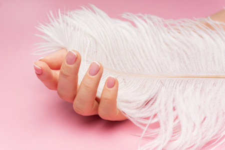 Closeup of female hand with smooth skin and soft ostrich feather on pink backgroundの写真素材
