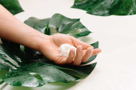 Closeup of female hand with a cleansing foam against tropical leaf backgroundの写真素材
