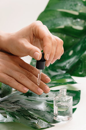 Closeup of female hands and bottle of nourishing cuticle oil with dropperの写真素材
