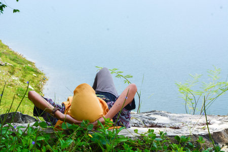 January 2, 2023, Wonosobo, Indonesia Portrait of a beautiful young Asian Muslim woman wearing a headscarf and glasses sitting alone. On a river bank. Smiling and happy expressionの写真素材