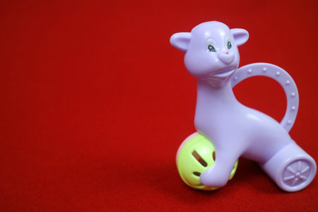 A toy shaped like an alpaca animal, purple in color, holding a ball. on a red background