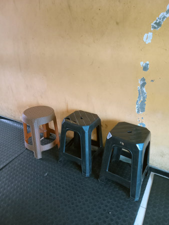 Three plastic chairs placed near a textured wall with peeling paintの写真素材