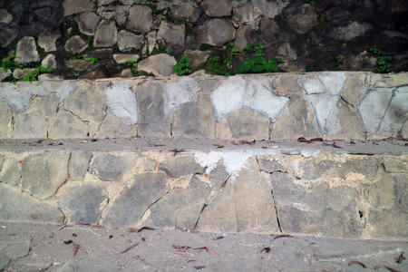 Aged stone steps showing cracks, dirt, and patch repairs with mossy backgroundの写真素材