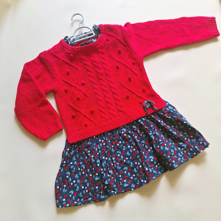 Adorable long sleeve red knitted baby dress featuring textured cable knit and bobble patterns on the top, paired with a soft navy floral skirtの写真素材