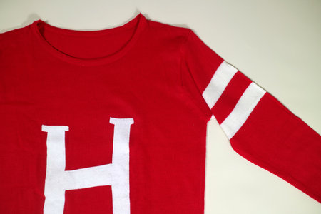 A red knitted shirt featuring white H letter and two white arm stripesの写真素材