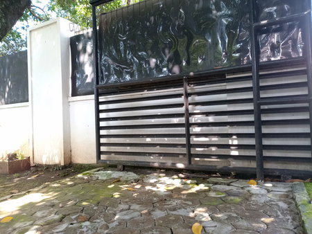 Black horizontal slatted gate stands with white concrete fence in sunny outdoor areaの写真素材