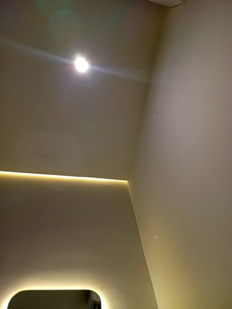 A close up view of a ceiling with a light fixture and ambient lighting along the edge. The wall is painted in a light color, creating a modern and minimalist atmosphere.の写真素材