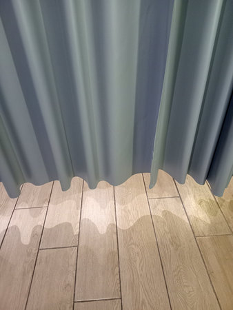 A close up view of soft, flowing curtains in shades of blue, casting gentle shadows on a wooden floor. The light creates a wavy pattern on the floor, enhancing the serene atmosphere.の写真素材