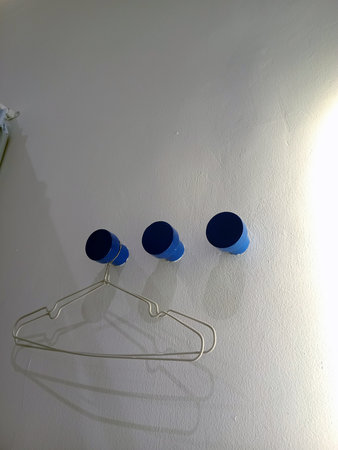 Three blue wall hooks mounted on a light colored wall, with a metal hanger hanging below them.の写真素材