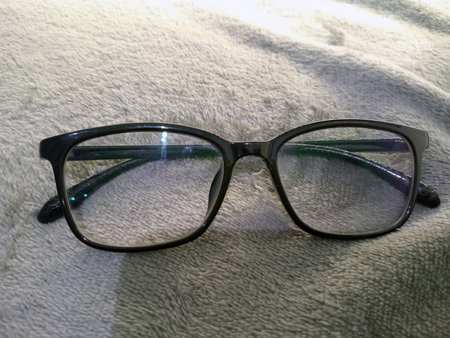 A pair of stylish black eyeglasses with square frames resting on a soft, textured surface. The lenses are clear, reflecting light.の写真素材