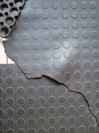 Close up of black rubber flooring with a textured surface, showing a tear in the material. The flooring features circular patterns and a contrasting edge from another rubber piece.の写真素材