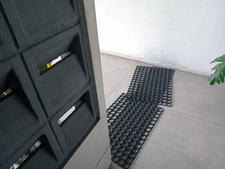 A view from an entrance showing two black rubber mats on a tiled floor, leading towards a wall. The setting is minimalistic with a clean, modern aesthetic.の写真素材