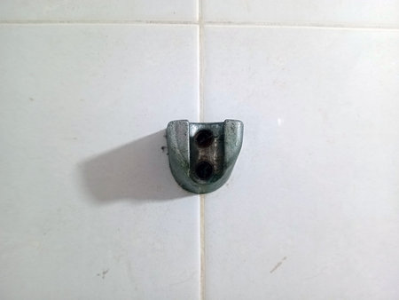 A close up view of a metallic wall fixture mounted on white tiles. The fixture has two holes for screws and a curved shape, suggesting it may be a bracket or support for hanging items.の写真素材