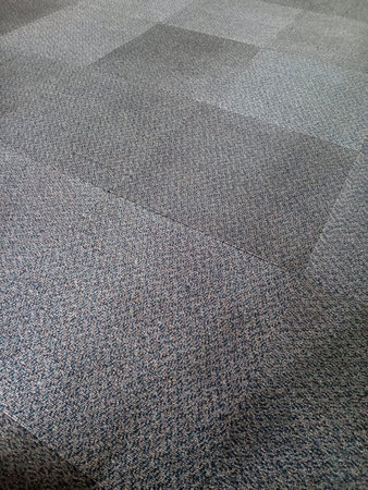 A close up view of a textured carpet floor featuring a pattern of squares in various shades of gray...