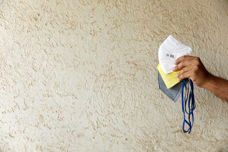 Man holding three types of Respirators. N95, FFP3 (Yellow), FFP1 (Gray) against a textured beige background with negative space on left for textの写真素材