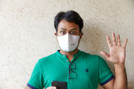 Man wearing a Green T-shirt holds a cell phone while looking surprisedの写真素材