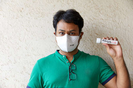 A colored man wearing a Green t-shirt holds a COVID Negative (COVID -ve) blood sample bottleの写真素材
