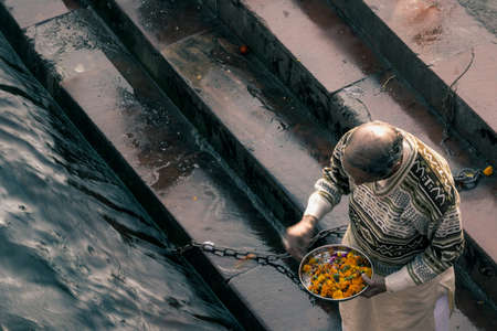 An old man with hidden face throwing flowers into the river Gangaの写真素材